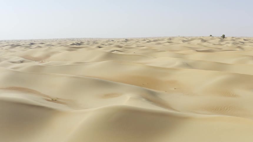 Sand dunes cover the desert under a blue sky