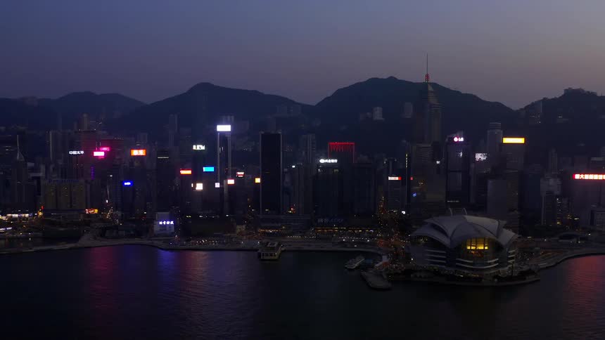 Skyline of the city with tall buildings and illuminated sign boards next to the sea at dusk