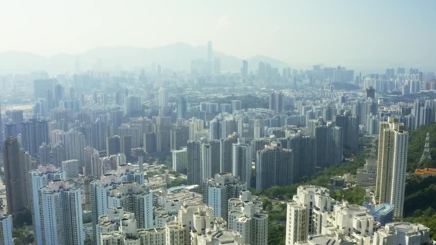 An urban area with densely packed skyscrapers lies before a large hill