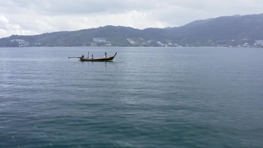 A small boat with 3 people in it is in the ocean away from the shoreline