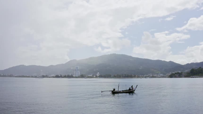 Two men fish from boat in water surrounded by mountains near town