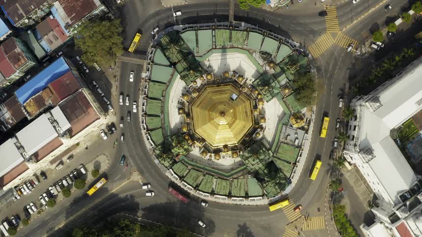 Cars and trucks travel around a golden burmese stupa in yangon