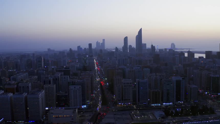 Buildings in a city sit under a darkening sky as traffic travels on the streets