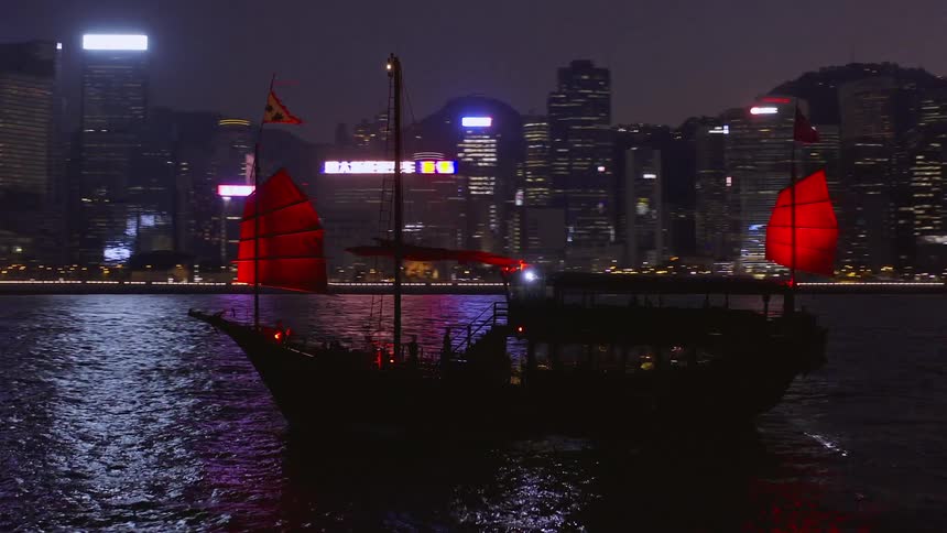 A red sail junk boat travels in victoria harbour hong kong at night