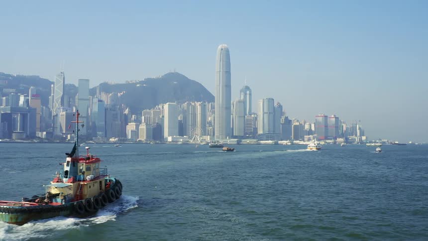Boats sail to the city with tall buildings and skyscrapers on a sunny day
