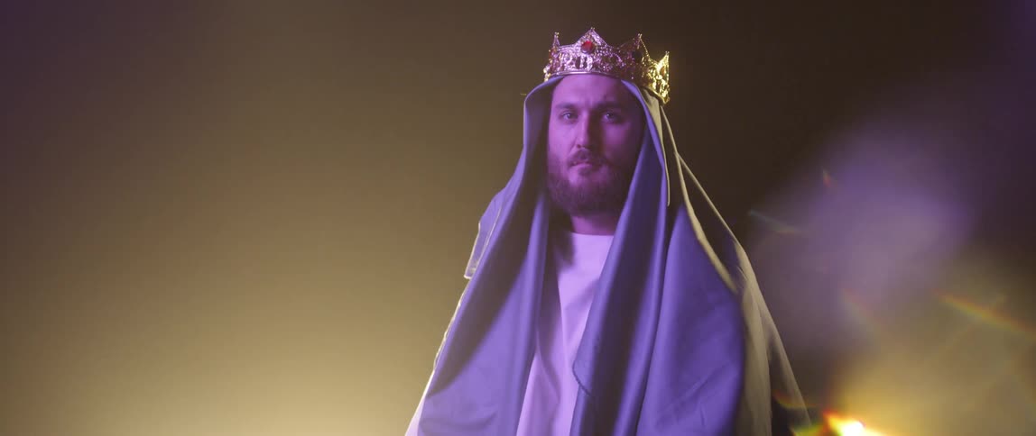 Man in crown and head covering glances up with backlighting