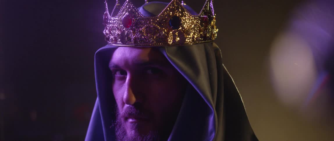 A man with a headcover and a crown staring off into the distance