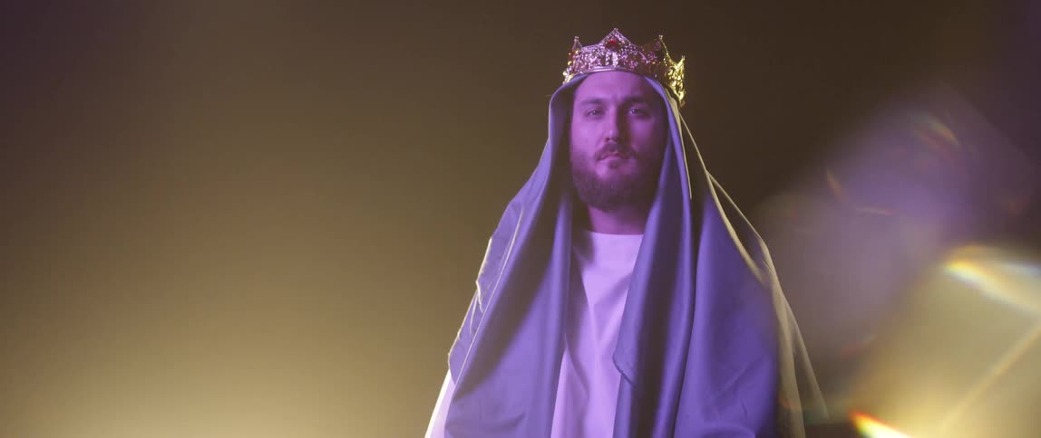 A man with a head covering and a crown staring