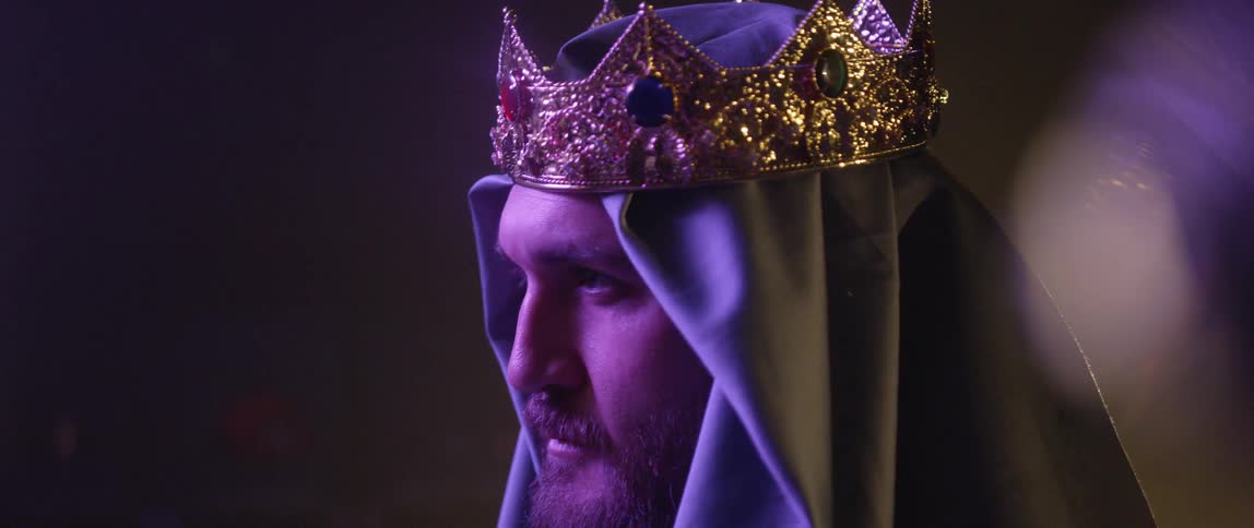 A man with a head covering and a crown looking off in the distance