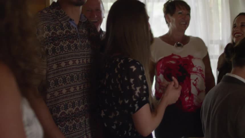 People smiling and singing in a house while a man plays the piano