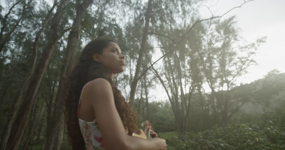 Black woman standing in the forest plays a guitar and turns around during the daylight
