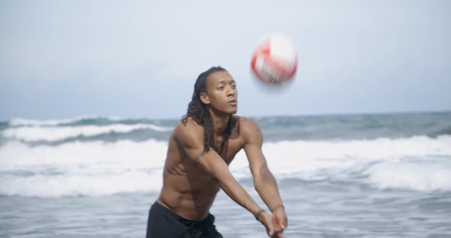 Shirtless muscular black man plays beach volley on the beach next to the sea on a cloudy day