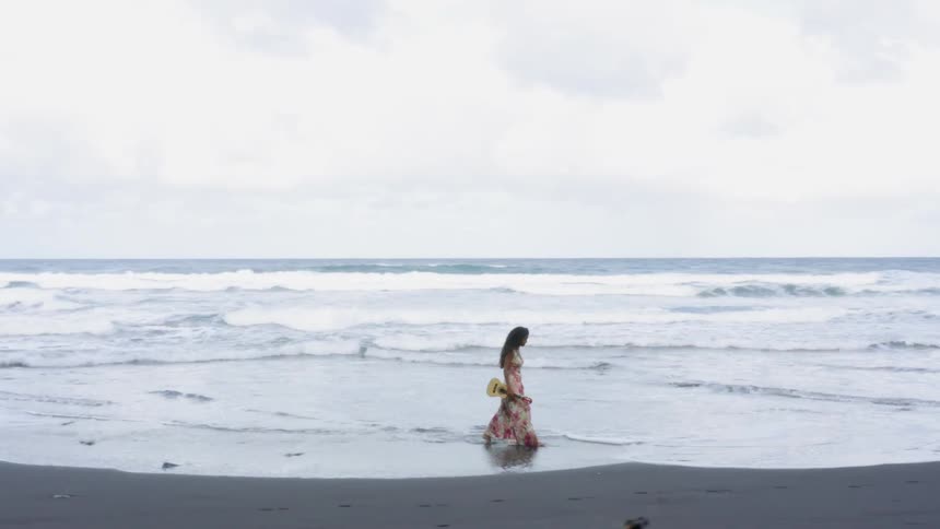 A woman walking on the beach with a white ukulele in her hand