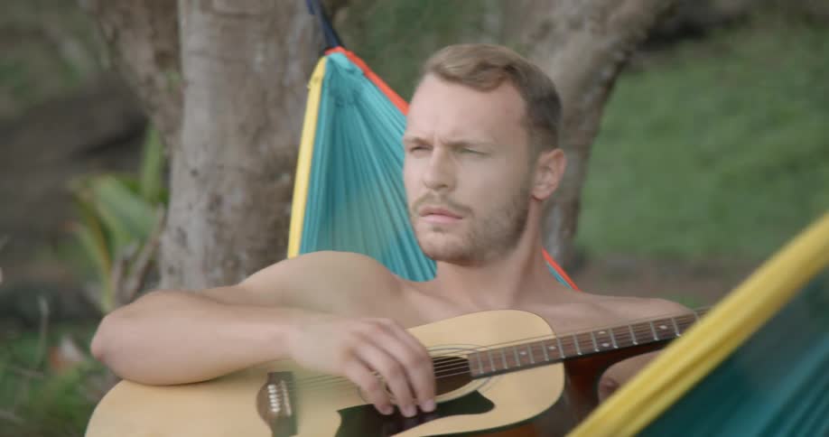 Male relaxing in a hammock playing the guitar