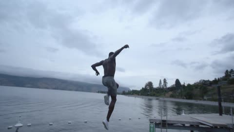 Man wearing shorts and sneakers jumps off of a high platform into a roped off portion of the lake