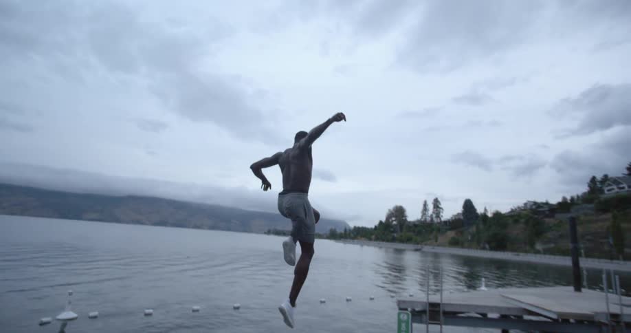 Man wearing shorts and sneakers jumps off of a high platform into a roped off portion of the lake