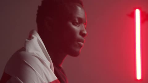 Black man holds up flag and covers himself in a room with red lights