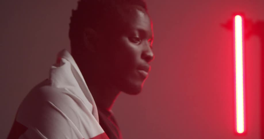 Black man holds up flag and covers himself in a room with red lights