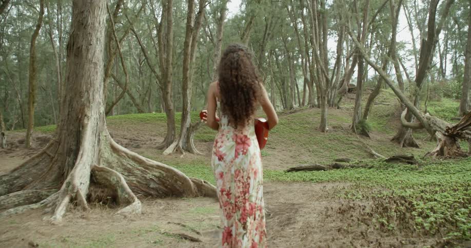 Curly haired brunette woman holding a guitar and walks in the forest track in the woods