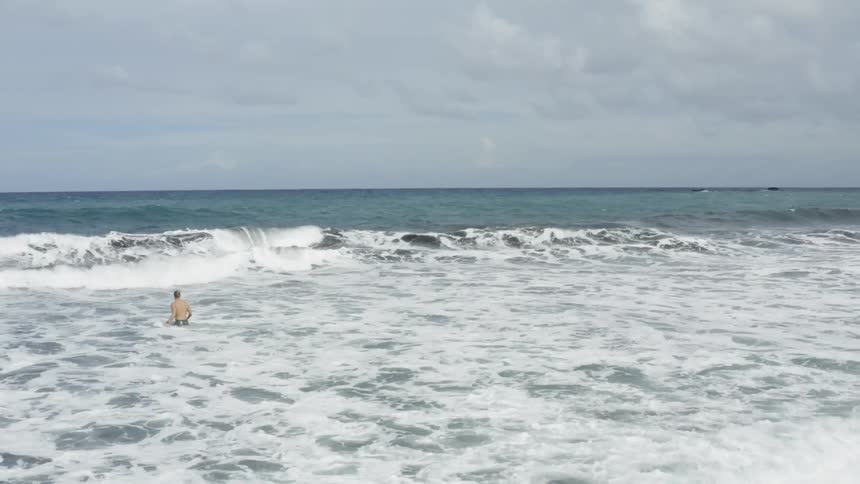Man walks out to sea through ocean with promontory in background
