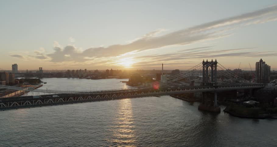 Cars and trucks travel on a city bridge over a river at sunrise