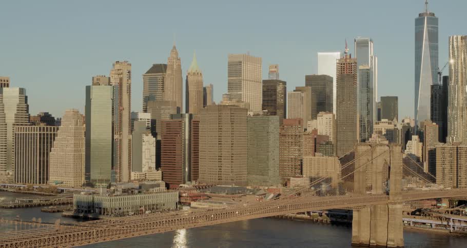 Cars travel across the brooklyn bridge with the manhattan skyline behind on a sunny day