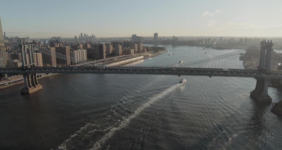 Several boats travel a river under a bridge between two cities