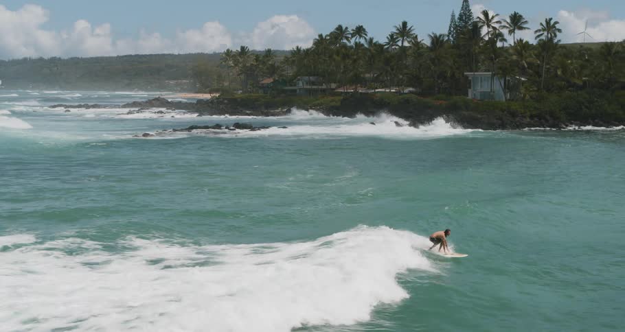A surfer rising into a stand on his surfboard on a small wave