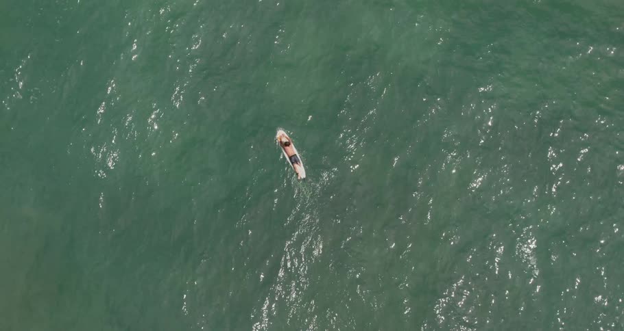Aerial of male surfer relaxing on a surfboard in the ocean