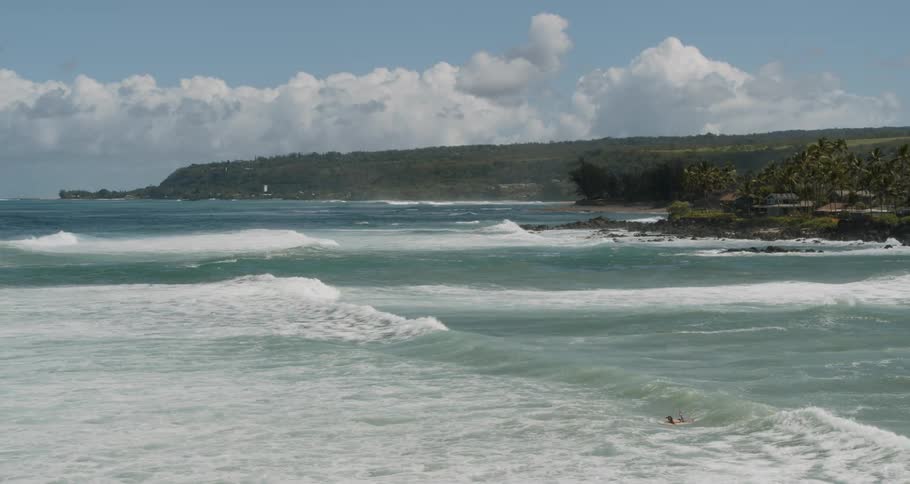 A person laying on a surfboard with waves and the sky in the background