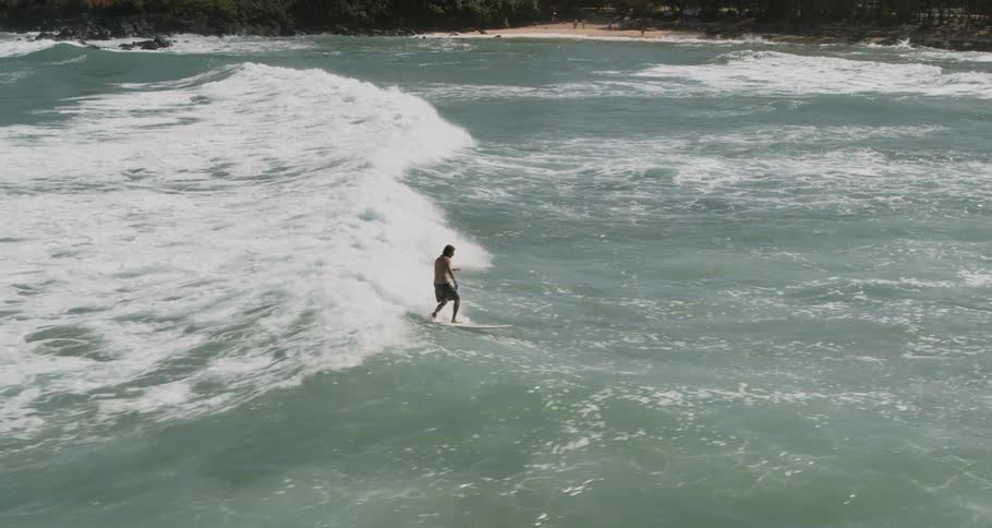 Male standing on a surfboard rides a wave towards the shore