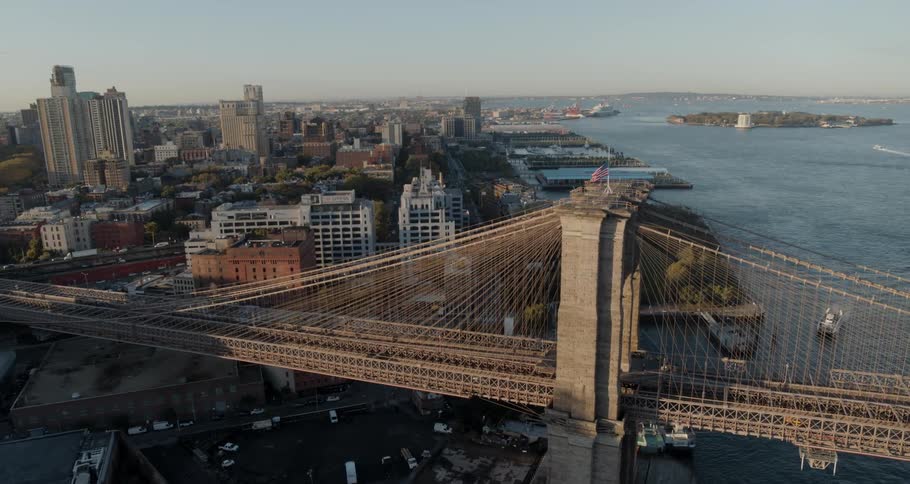 An american flag flies high atop a city bridge with traffic crossing over the harbor