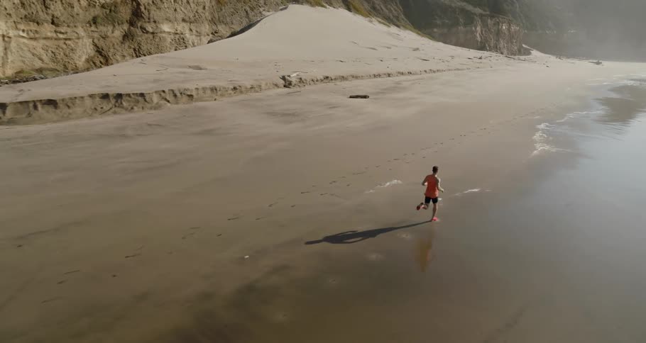 Man running on the sand alongside the shoreline in a bay