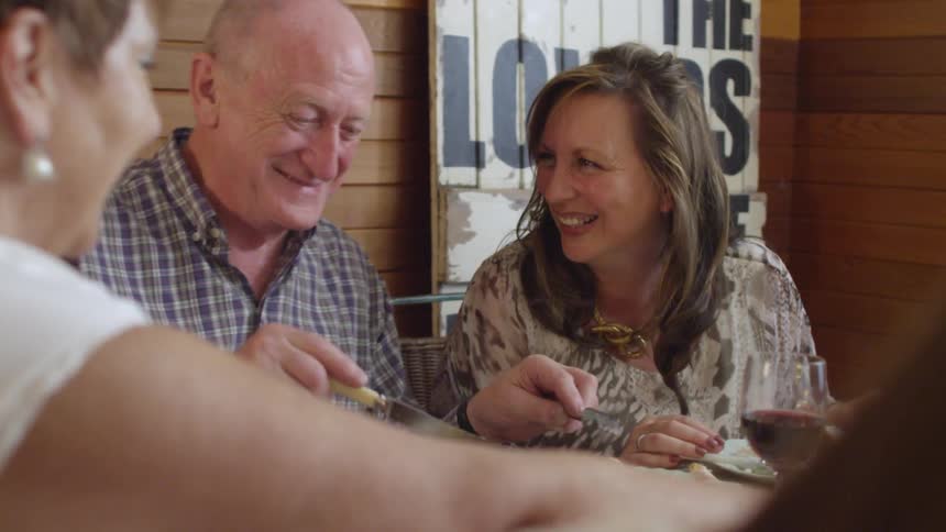 A family is seated at a table eating and enjoying each other's company while talking and laughing