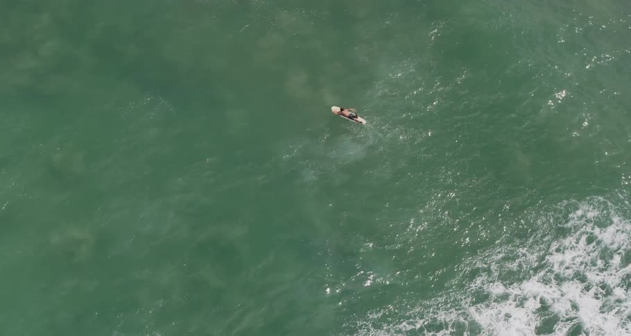 Birds eye view of surfer paddling over swells in the ocean