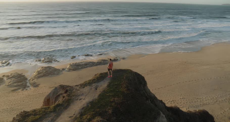 Man stands on a hill looking out at the ocean on a sunny day