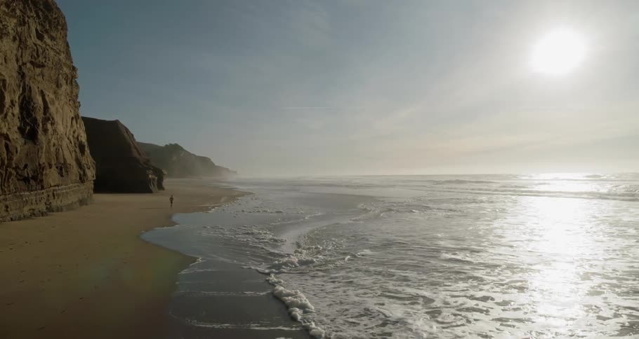 Man runs on the wet sand beach next to the ocean in the afternoon