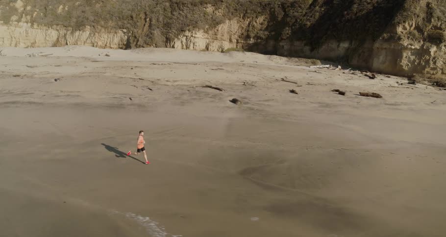 Aerial of a man running on the sand alongside the shoreline in the bay