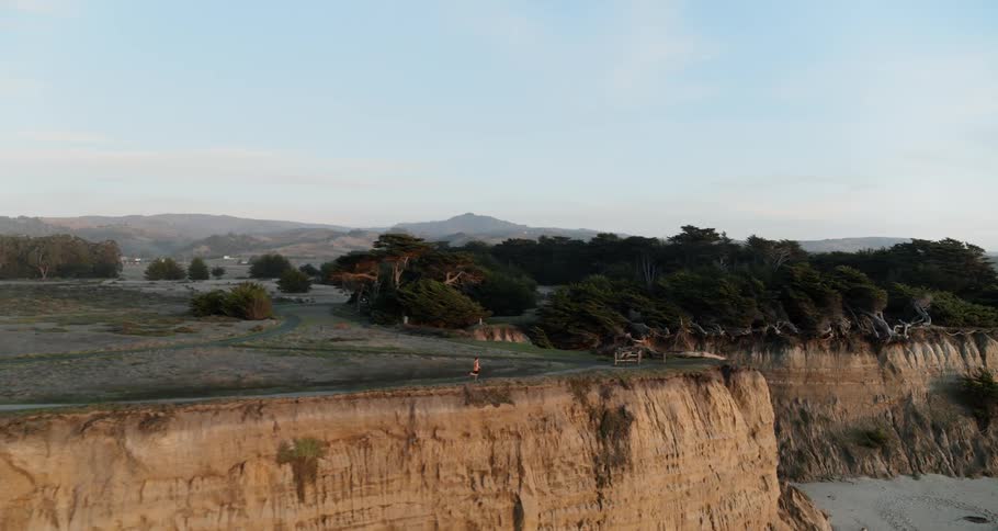 Aerial of a man running on a cliffside trail on the coast