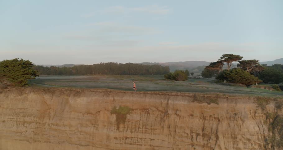 Aerial of a runner running on a trail alongside a cliff