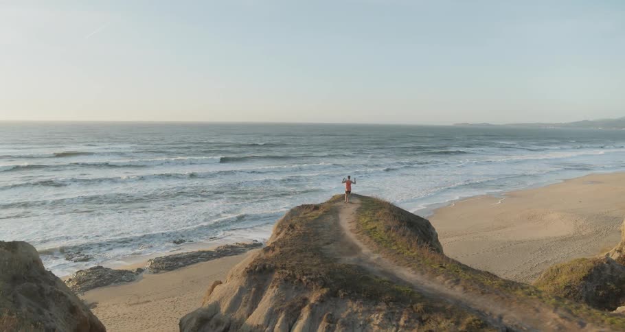 Male running to end of trail on top a cliff on the coast and celebrating