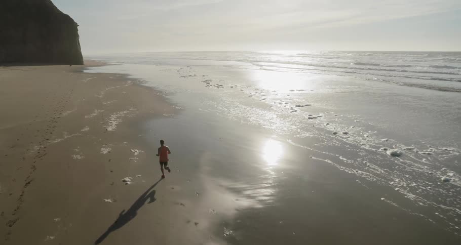Man runs on the wet sand beach next to the ocean