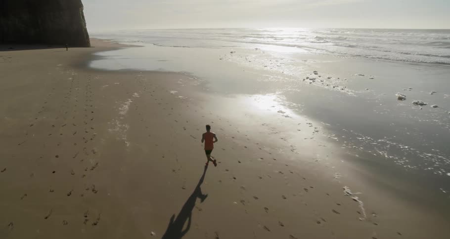 A man jogs along a deserted beach leaving footprints in the sand