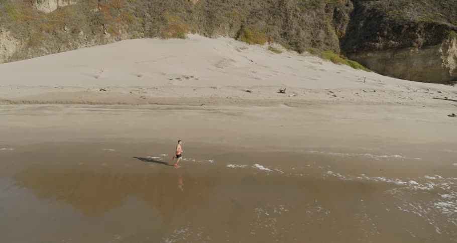 Man jogs along the beach next to the ocean in the daytime