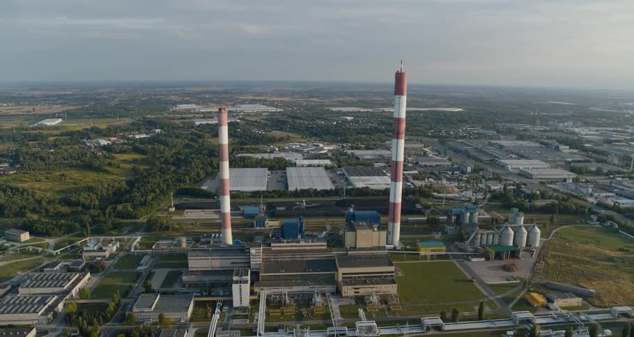 Two red and white smoke stacks rise from an industrial building in a metropolitan area