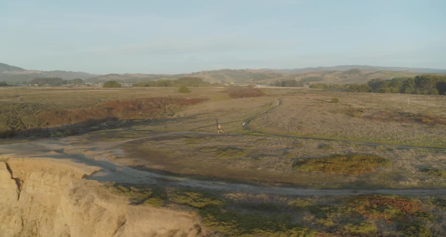 Aerial view of man running up to the cliffside on a sunny day