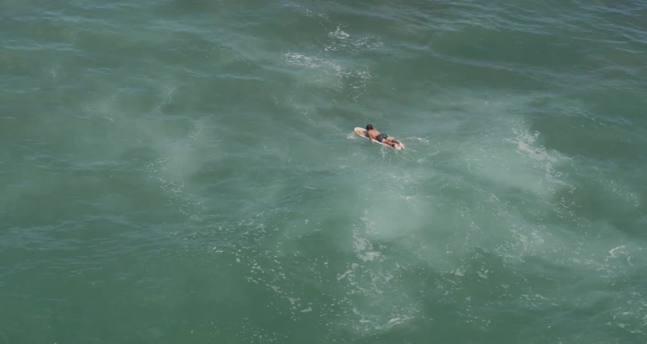 Aerial of a surfer paddling over swells in the ocean