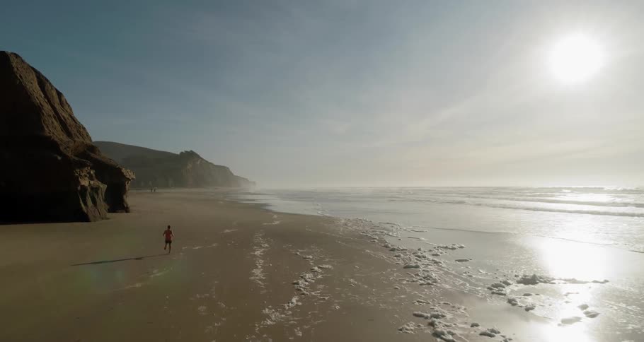 Man runs on the wet sand beach next to the ocean in the afternoon