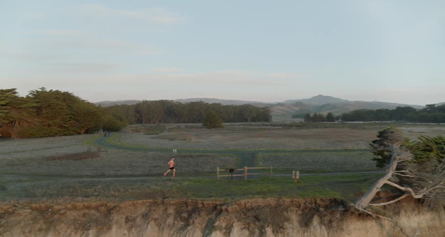 A man running on a dirt road with trees and the sky in the background