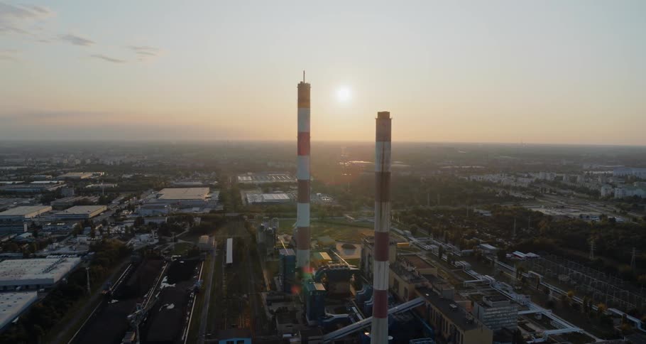 Two red and white smoke towers stand above an industrial area against a rising sun